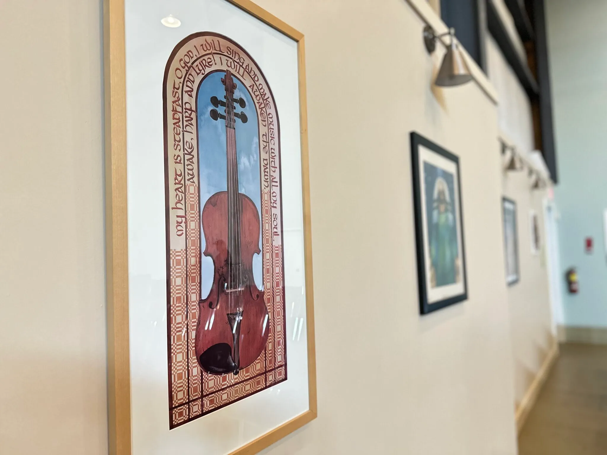 Framed violin artwork along a church hallway wall